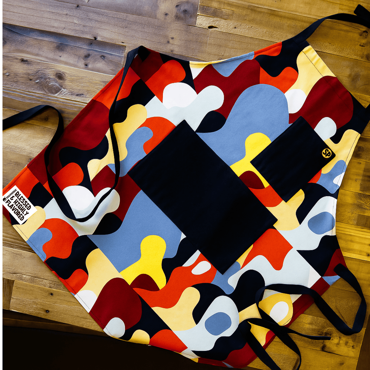 beryl apron with red, blue, gold, and black abstract print, laid flat